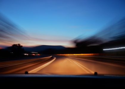 A motion-blurred highway at dusk seen through a car windshield