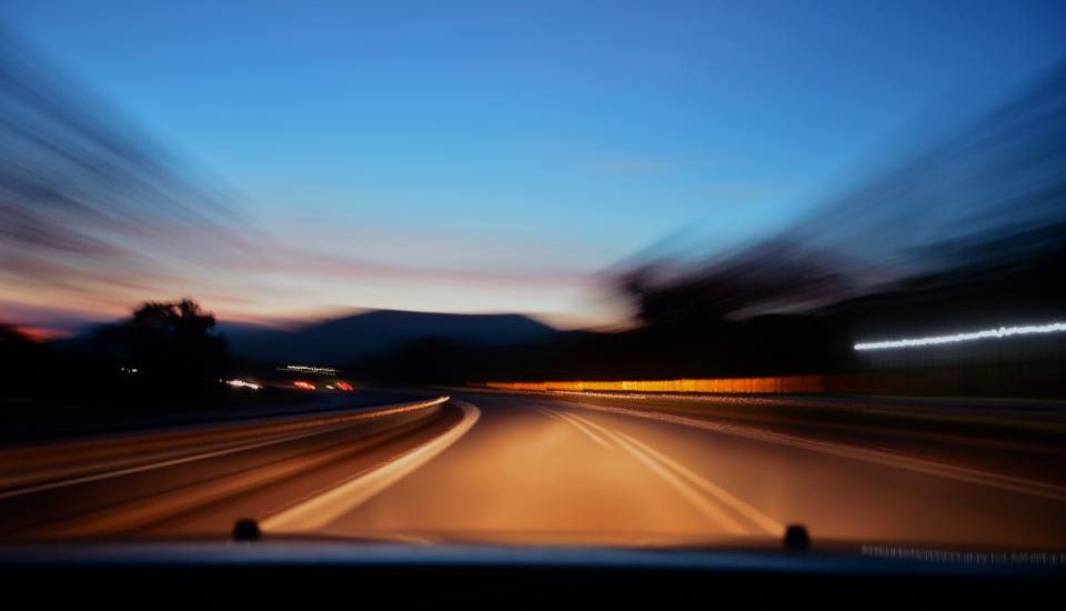 A motion-blurred highway at dusk seen through a car windshield