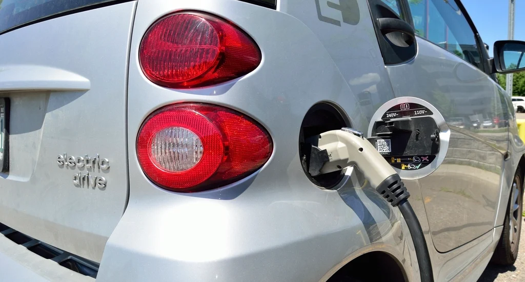 A small silver electric car plugged in at a charging station