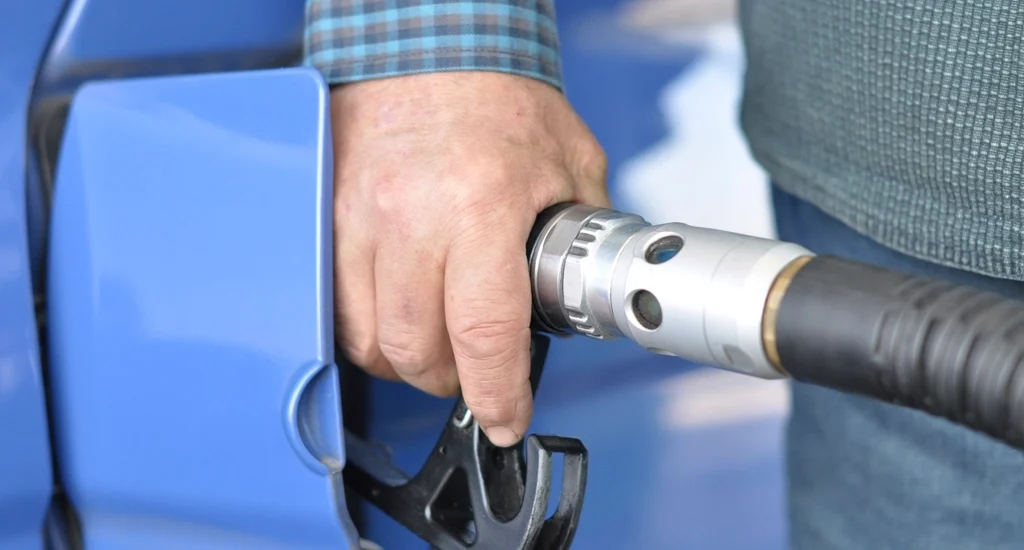 A hand holding a fuel nozzle at a car's filler